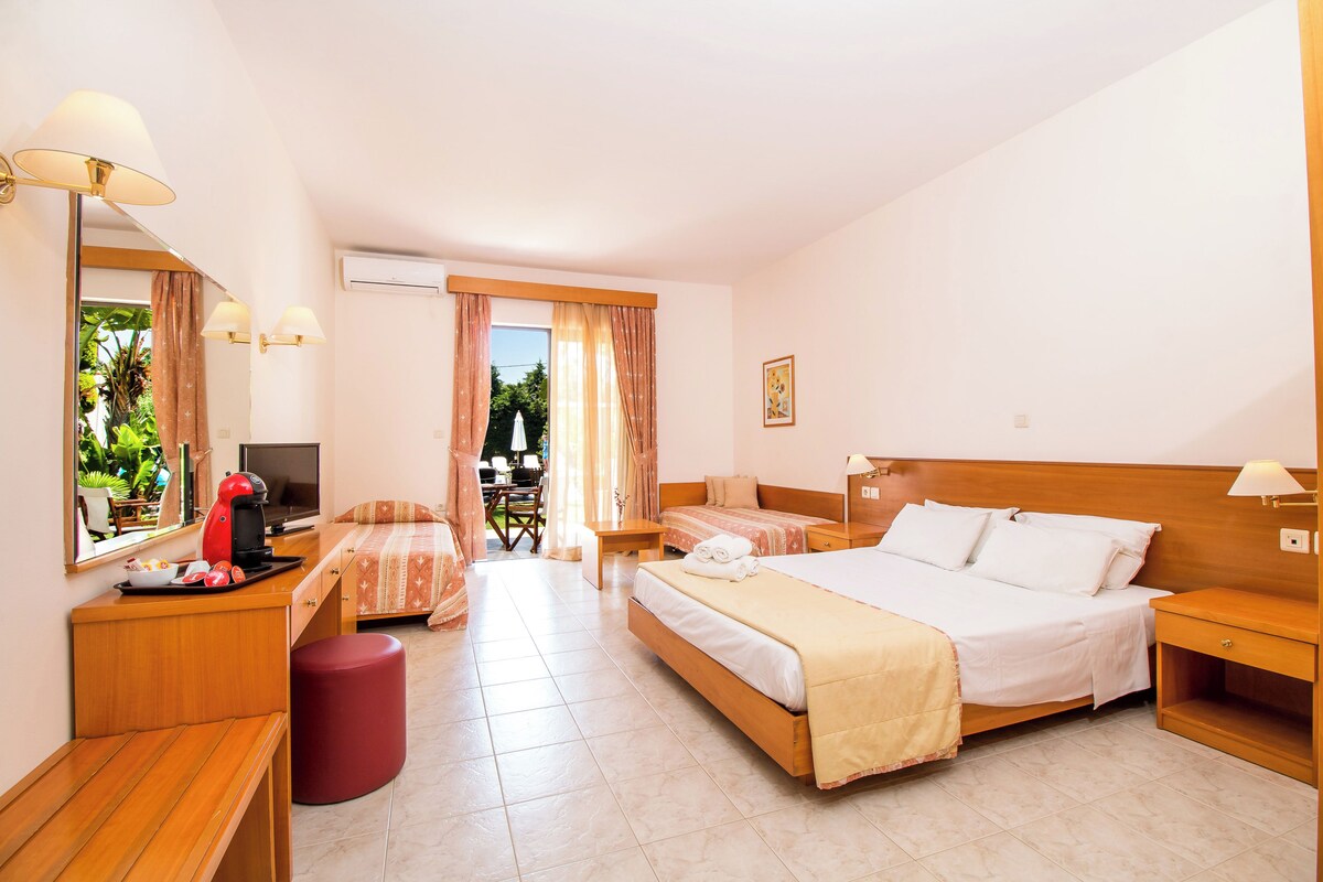 Ein Hotelzimmer mit einem Bett, einem Schreibtisch mit Computer, einem Stuhl und einem kleinen Tisch mit Lampe.