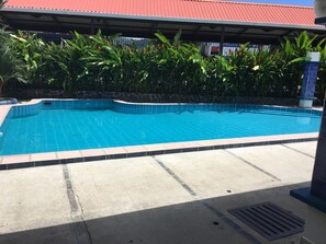 A swimming pool with blue tiles, surrounded by a stone wall and tropical plants. - Apartotel Gaviotas (Jacó)