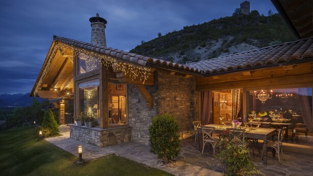 A stone house with a tiled roof, a chimney, and a dining area with outdoor seating.