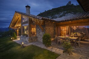 A stone house with a tiled roof, a chimney, and a dining area with outdoor seating. - Hotel Viñas de Lárrede (Sabinanigo)