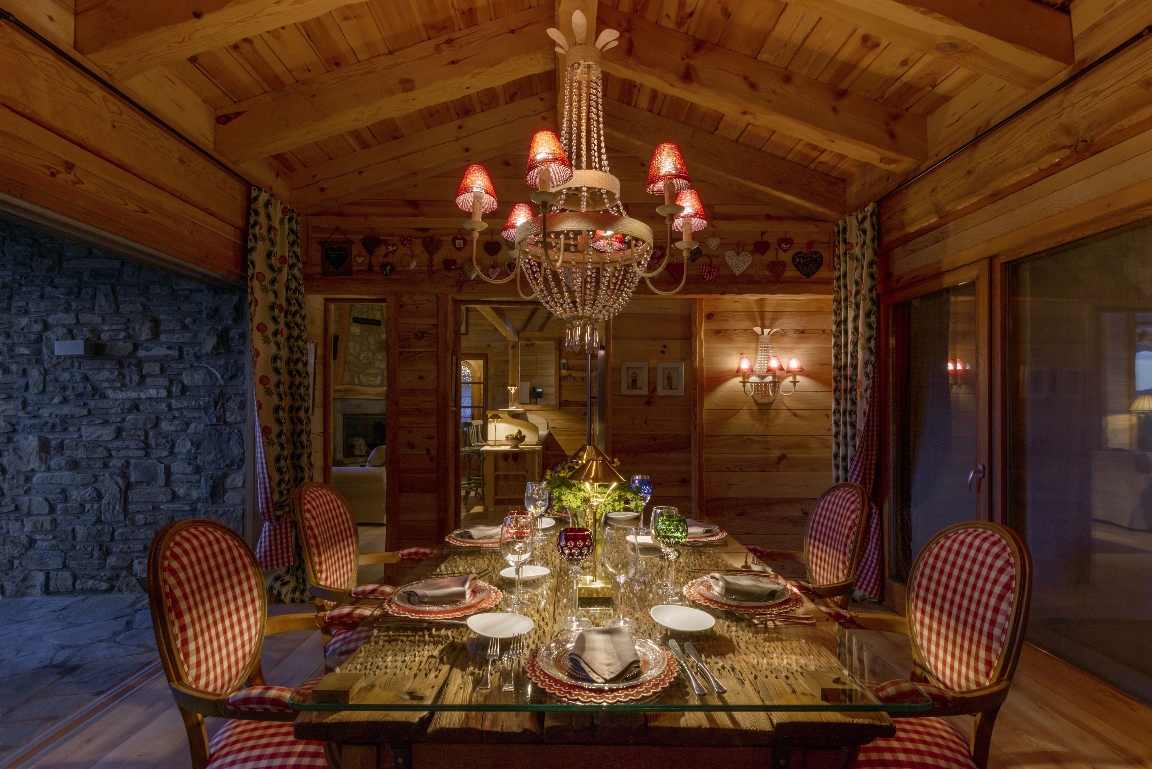 Comedor de madera con candelabro, sillas a cuadros y una mesa de vidrio dispuesta para una comida.