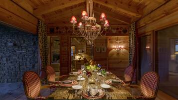 Comedor de madera con candelabro, sillas a cuadros y una mesa de vidrio dispuesta para una comida.