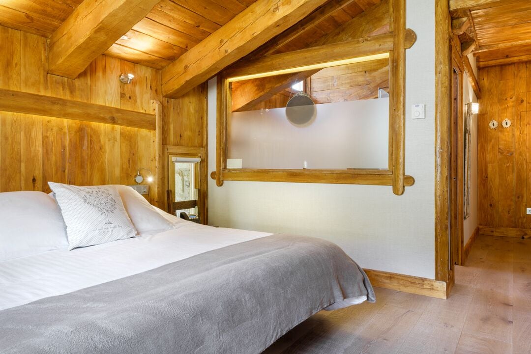 A wooden room with a bed, a window with a frosted glass panel, and a wooden ceiling.