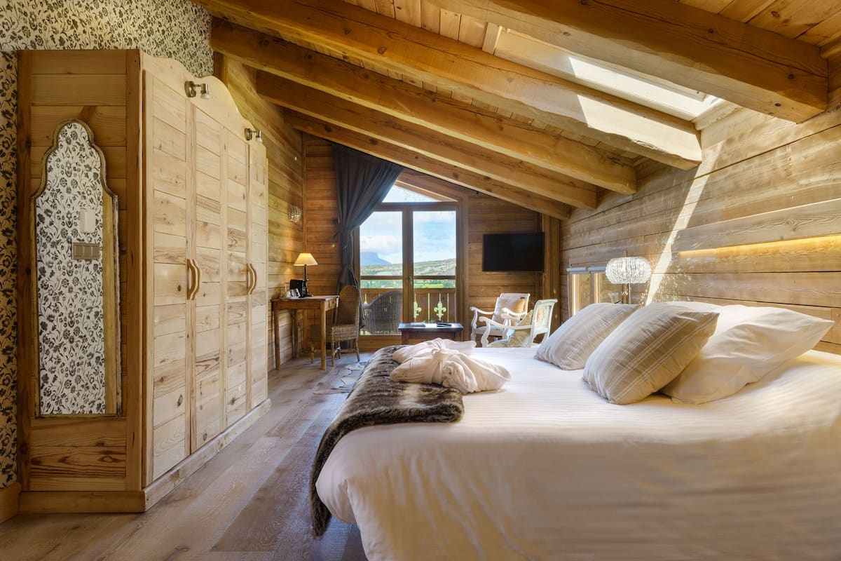 Een houten slaapkamer met een bed, twee stoelen, een bureau en een televisie.