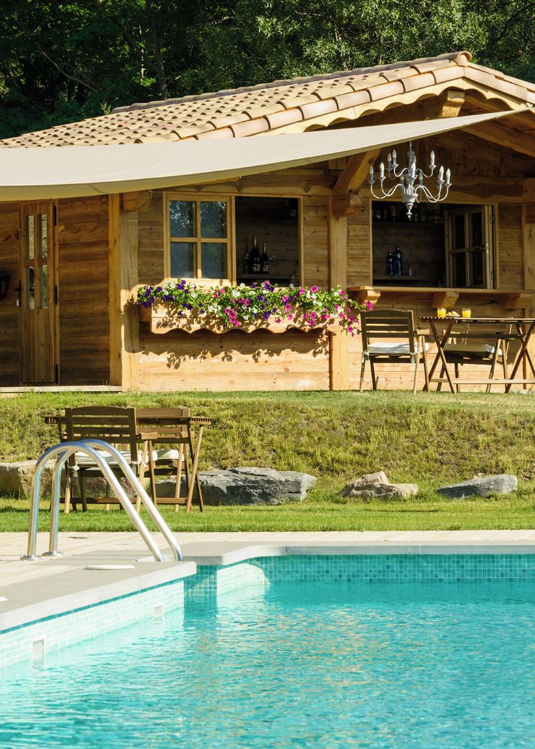 Una cabaña de madera con piscina, mobiliario exterior y una jardinera con flores.
