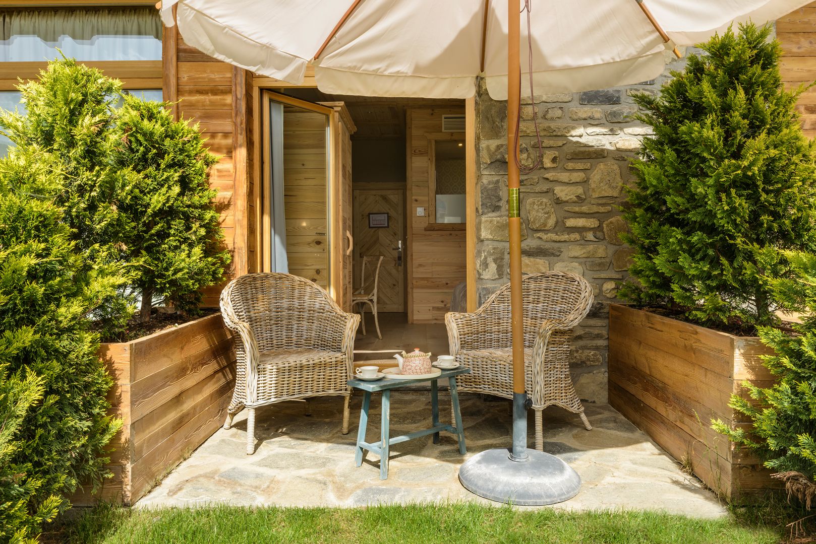 A wooden cabin with two wicker chairs and a table under a canopy.