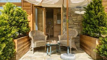 A wooden cabin with two wicker chairs and a table under a canopy.