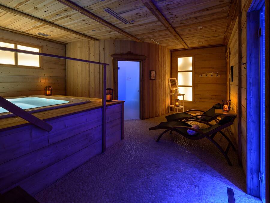 A wooden cabin with a hot tub, two lounge chairs, and a small table with a lantern.