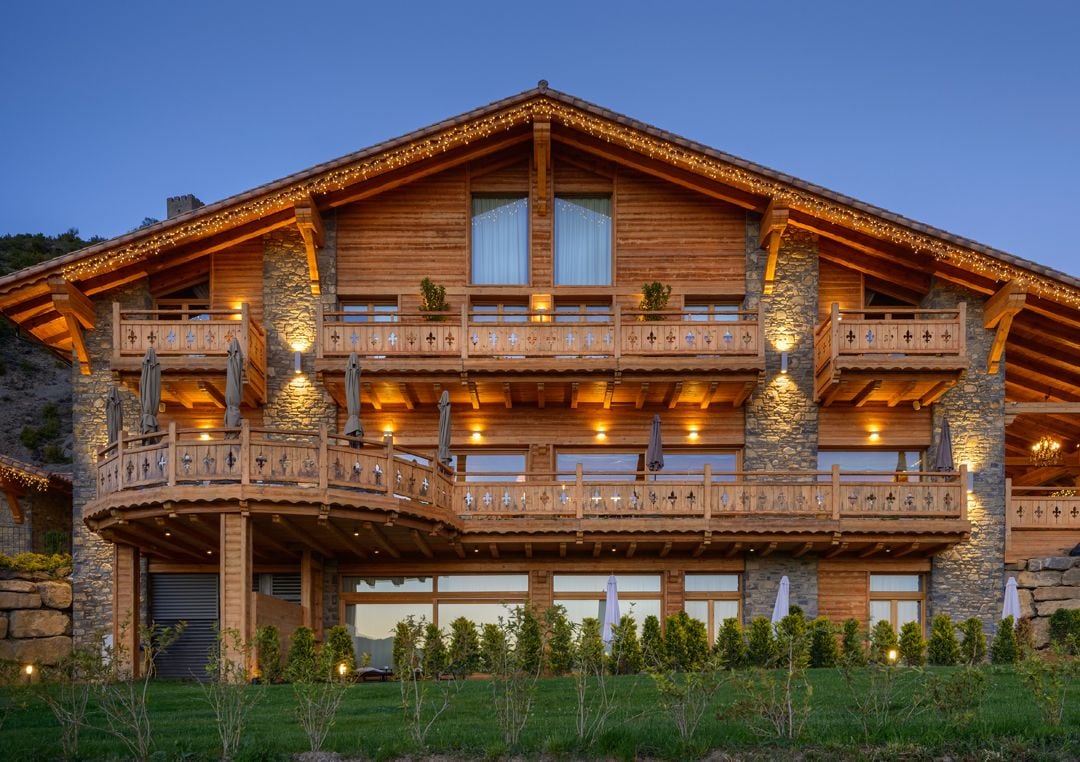 Eine große Holzhütte mit mehreren Balkonen, Steinverzierungen und Außenbeleuchtung.