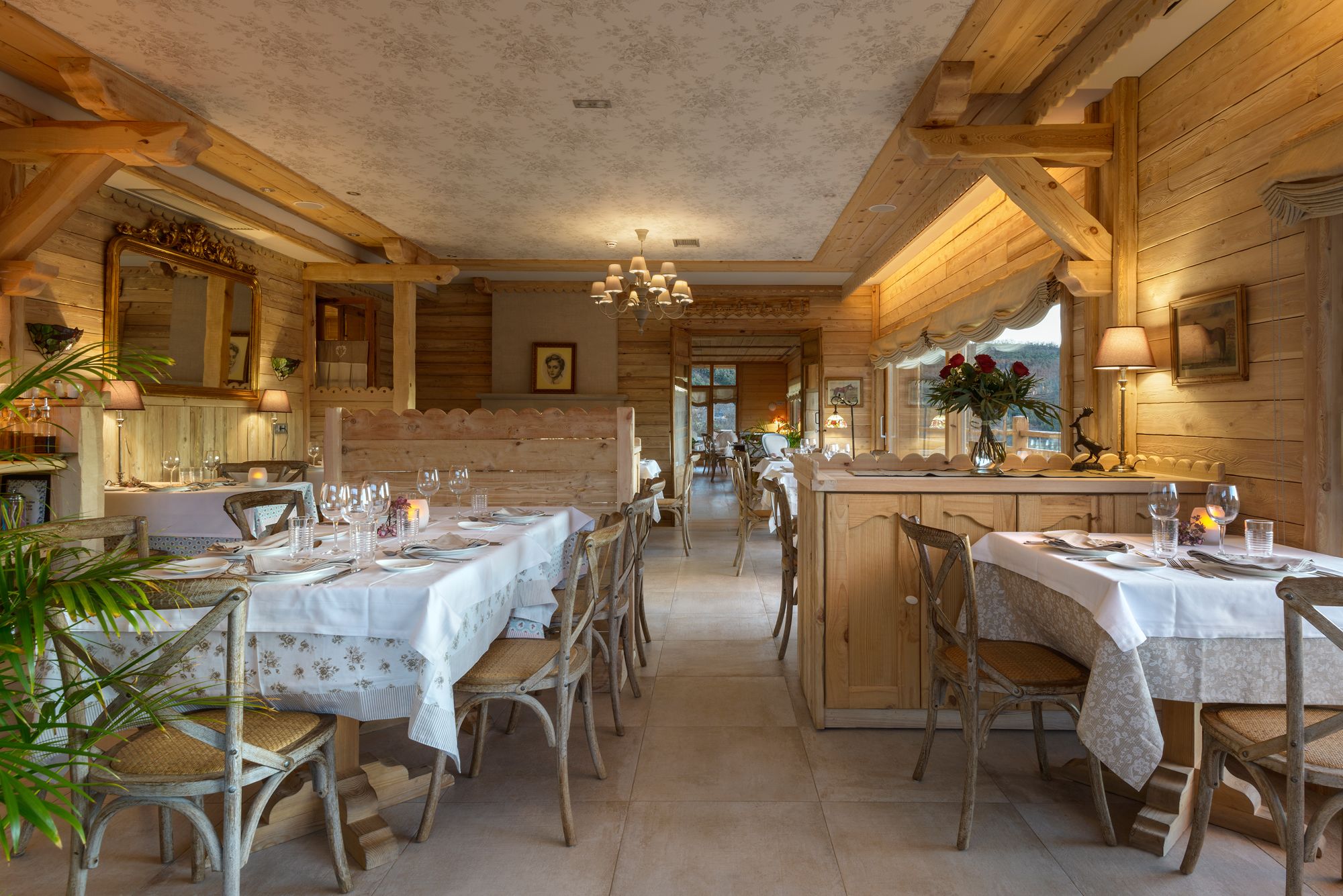 Un intérieur rustique en bois, avec de nombreuses tables à manger dressées pour accueillir les clients, des chaises en bois classiques et une ambiance chaleureuse et accueillante.