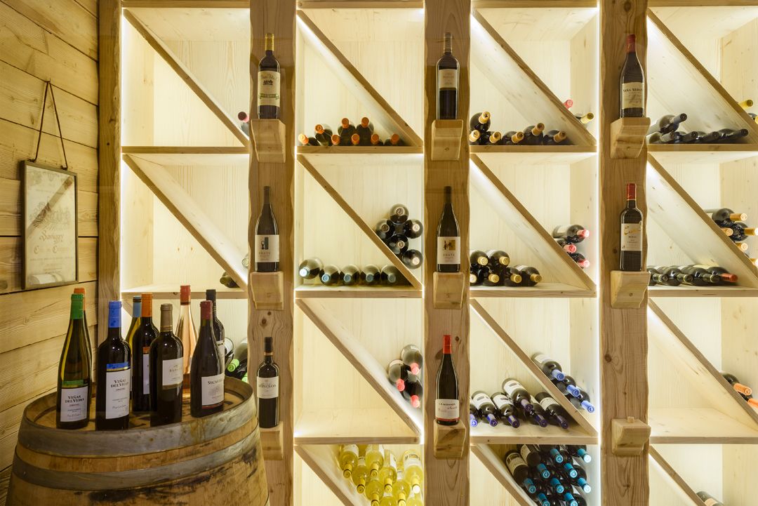 A wine cellar with wooden shelves and barrels, displaying various bottles of wine.