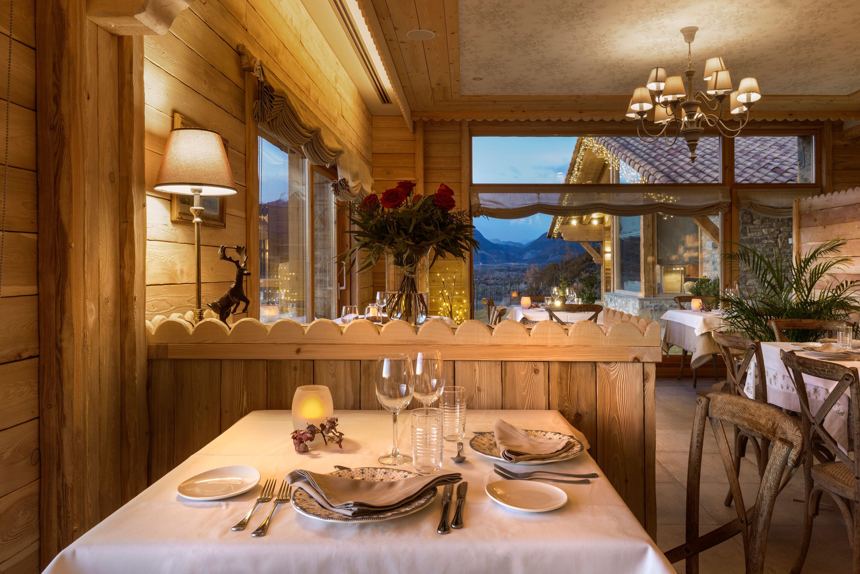 Un interior de madera con una mesa de comedor para cuatro, un jarrón de rosas rojas y vistas a montañas a través de amplios ventanales.