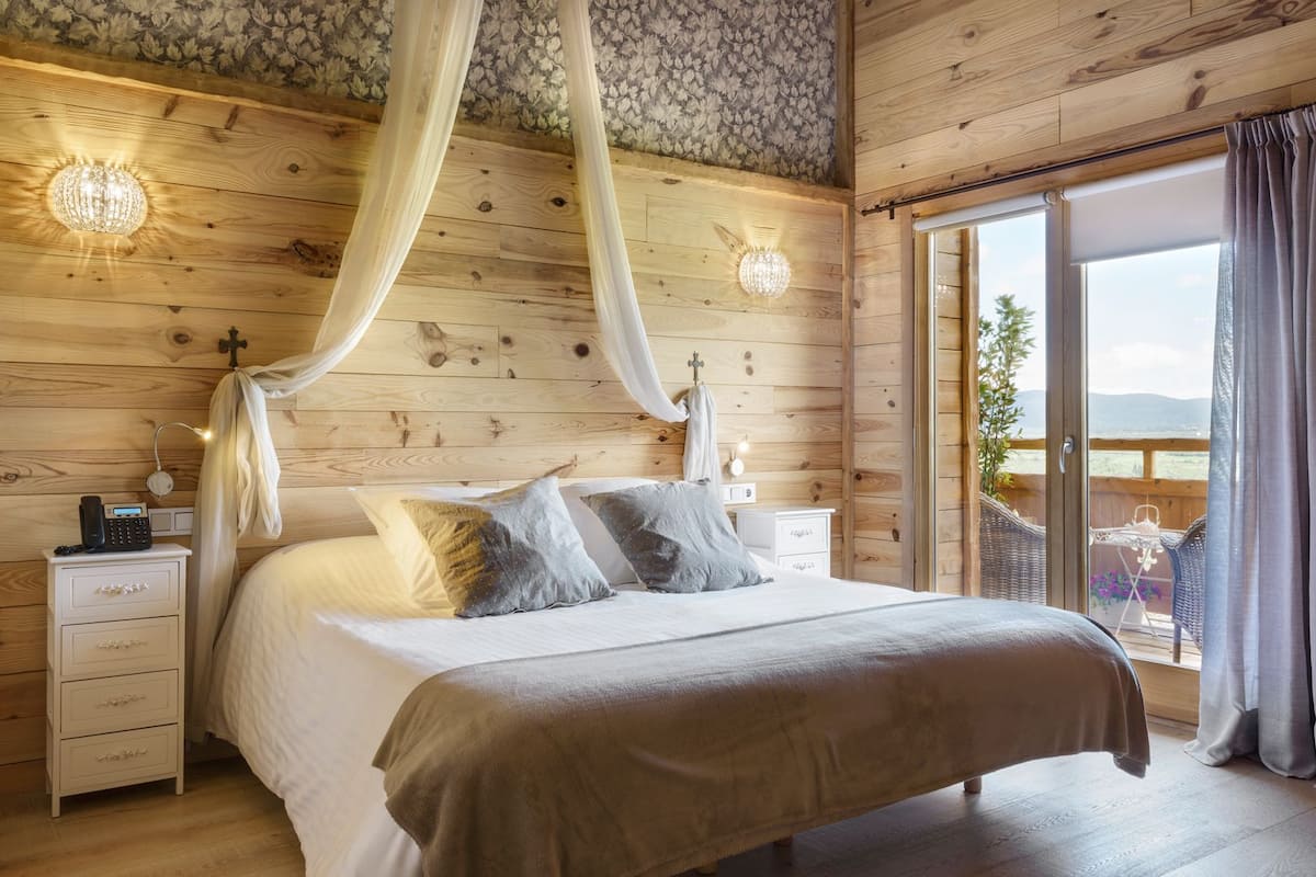 Een slaapkamer met hemelbed, houten wanden, een nachtkastje met telefoon en uitzicht op het groen.