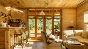 A wooden cabin interior with a bar area, seating, and a view of the outdoors.