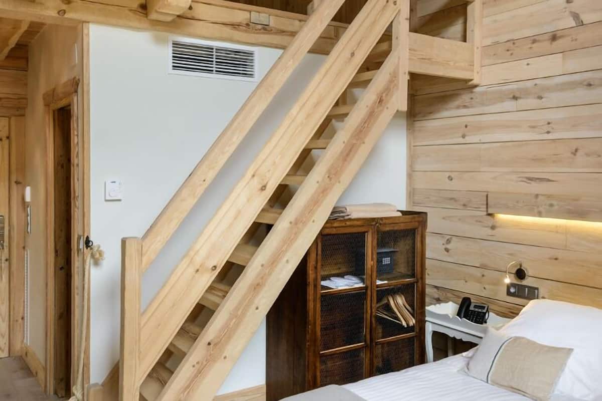 Een slaapkamer in een houten blokhut met een bed, een nachtkastje, een houten kast en een trap.