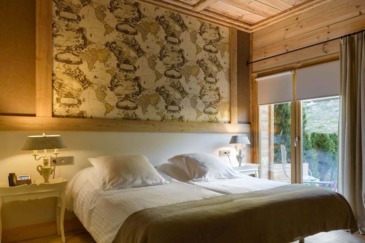 Slaapkamer met een grote muurcirkel, twee nachtkastjes met lampen, een bed met witte lakens en uitzicht op groen door een raam.