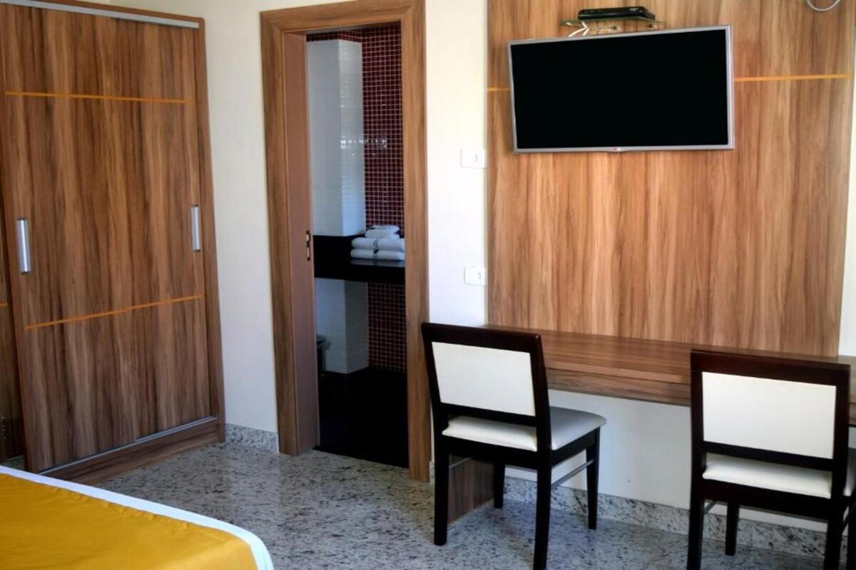 A room with a bed, a desk with two chairs, a TV mounted on the wall, and a wardrobe.