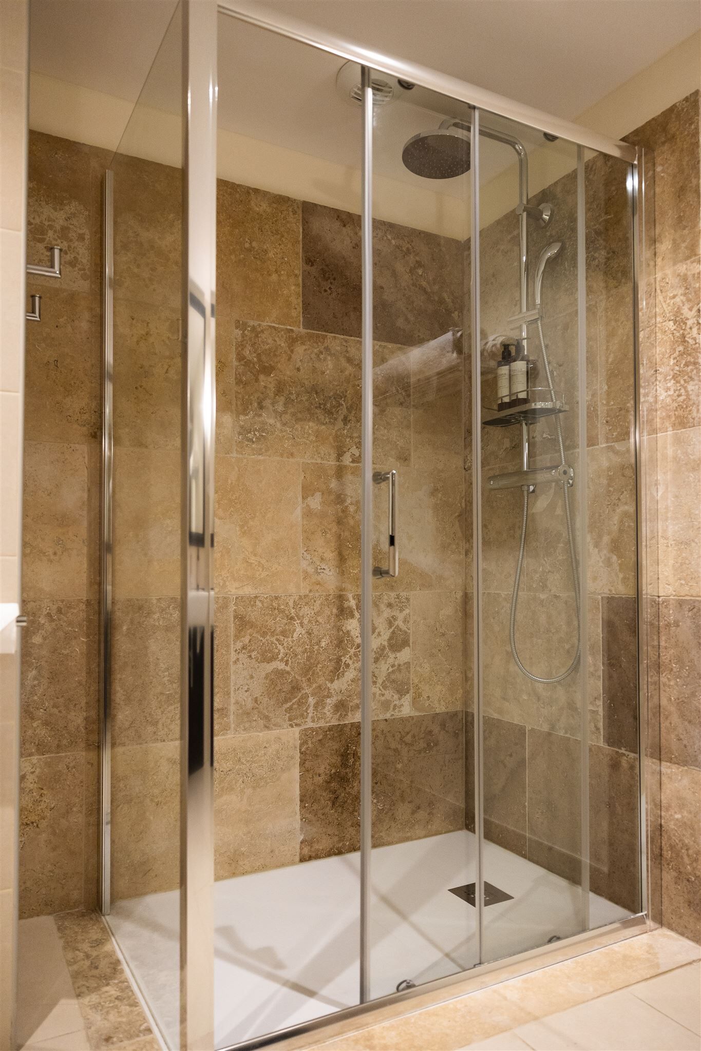 Cabina de ducha con paredes de vidrio, un cabezal de ducha de mano y un grifo de pared.