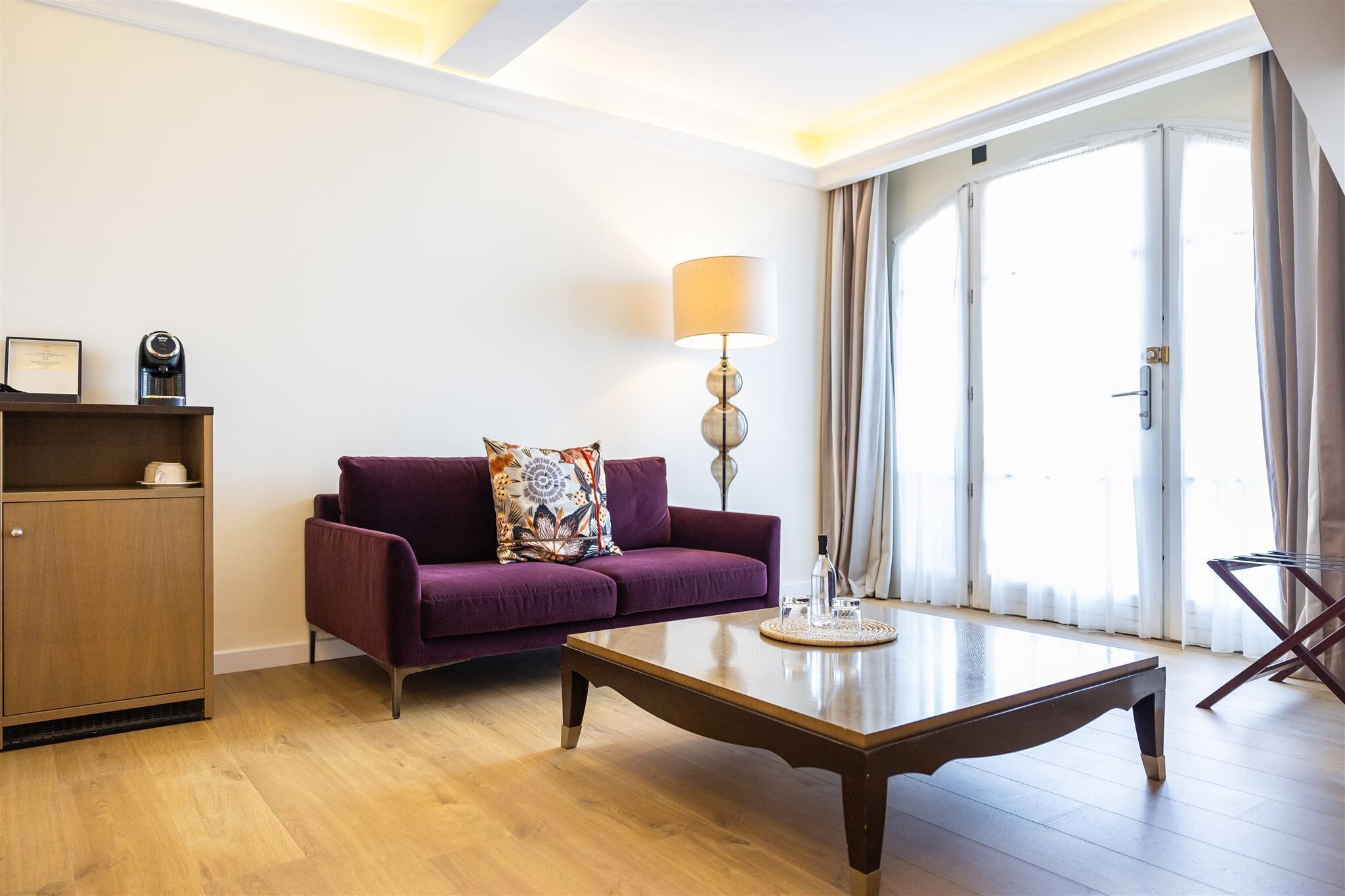 Una sala de estar moderna con una mesa de centro de madera, un sofá púrpura con un cojín decorativo, una lámpara de pie y un mueble de madera.