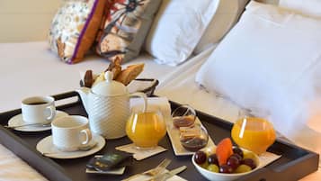 Uma bandeja de café da manhã com xícaras, suco de laranja e uma tigela de frutas sobre a cama, com almofadas.