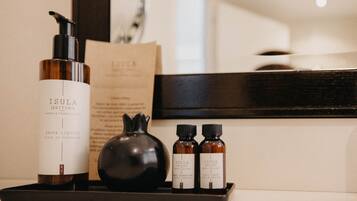 Un plateau avec un flacon de parfum Isula, une grenade et deux plus petits flacons, qui contiennent probablement des produits de soins pour la peau, dans un décor d’hôtel.