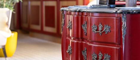 Un mueble de madera rojo con tiradores decorados, una pequeña estatua y un candelabro.