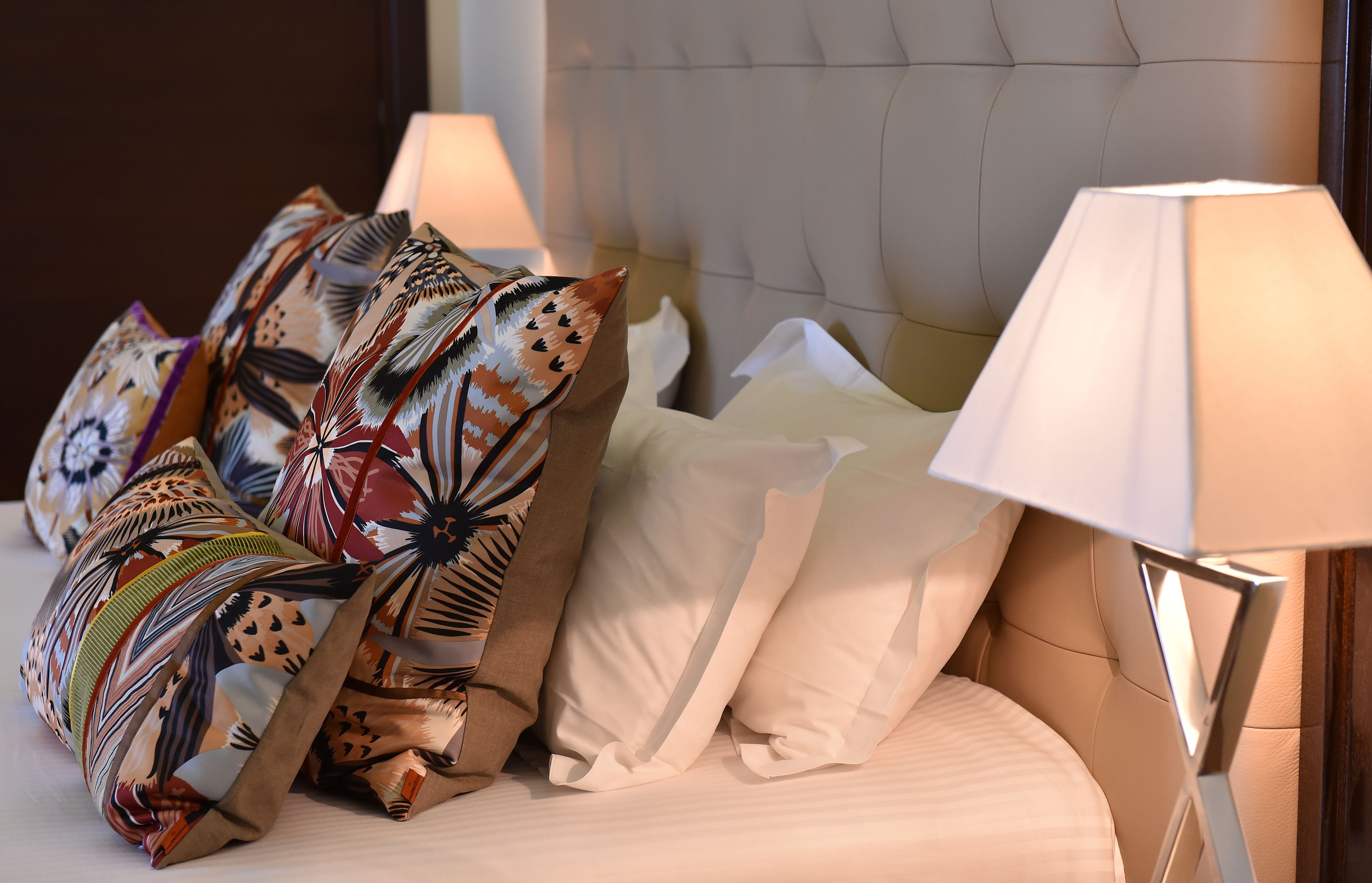 A bed with multiple pillows, including patterned and plain ones, and two bedside lamps.