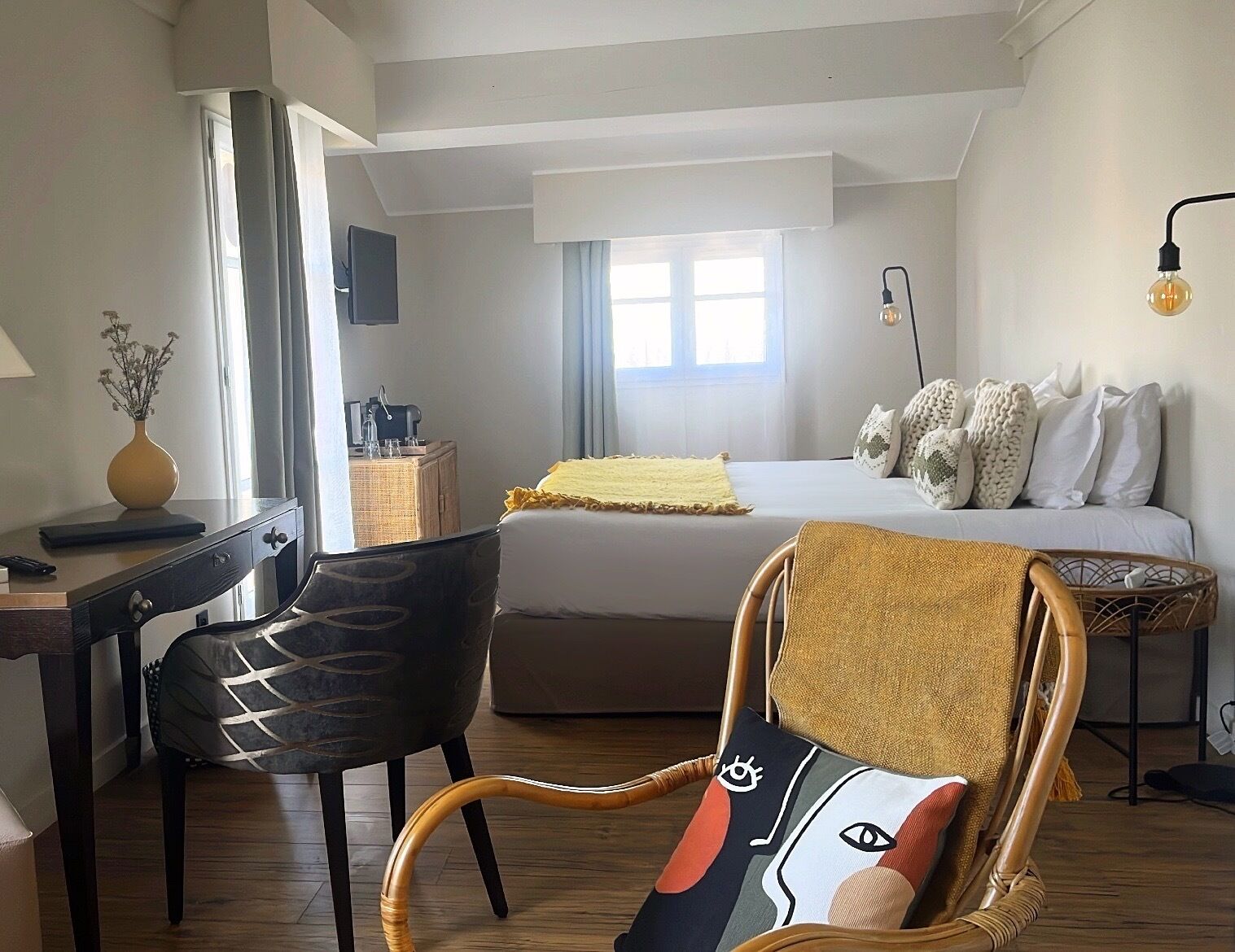A hotel room with a bed, a desk, a chair, a lamp, and a window.