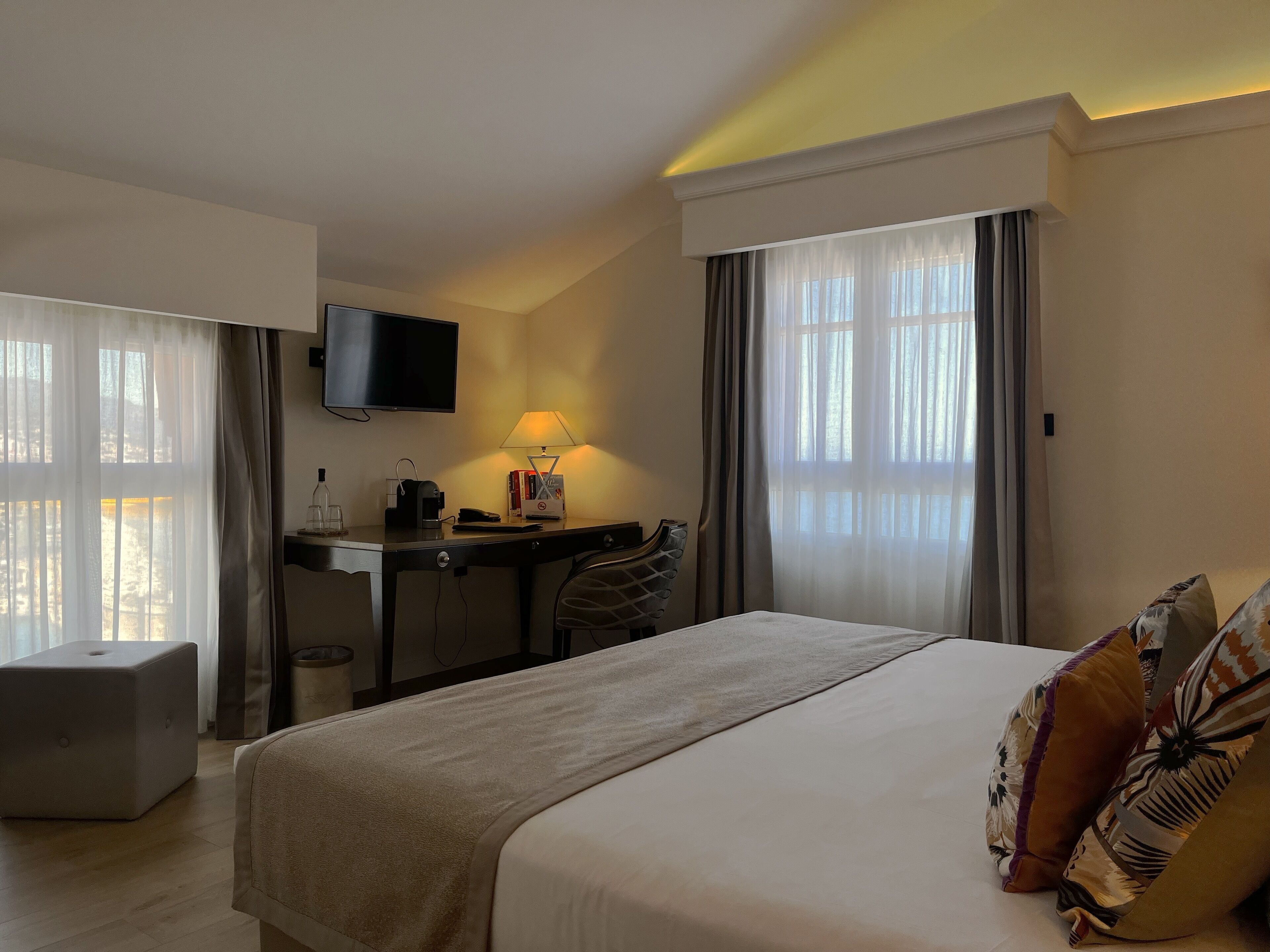 A hotel room with a bed, a desk, a chair, a TV, and a lamp.