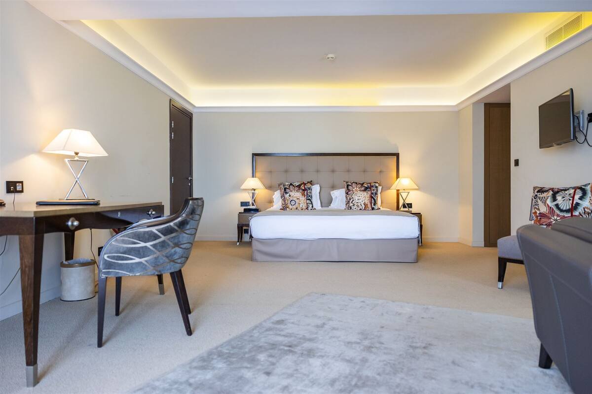 A hotel room with a bed, desk, chair, and a TV.