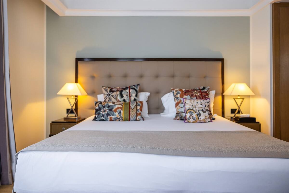 A hotel room with a large bed, two bedside tables with lamps, and a headboard with tufting.