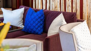 Een woonkamer met een houten scheidingswand, een paarse bank met witte en blauwe kussens en een witte fauteuil.