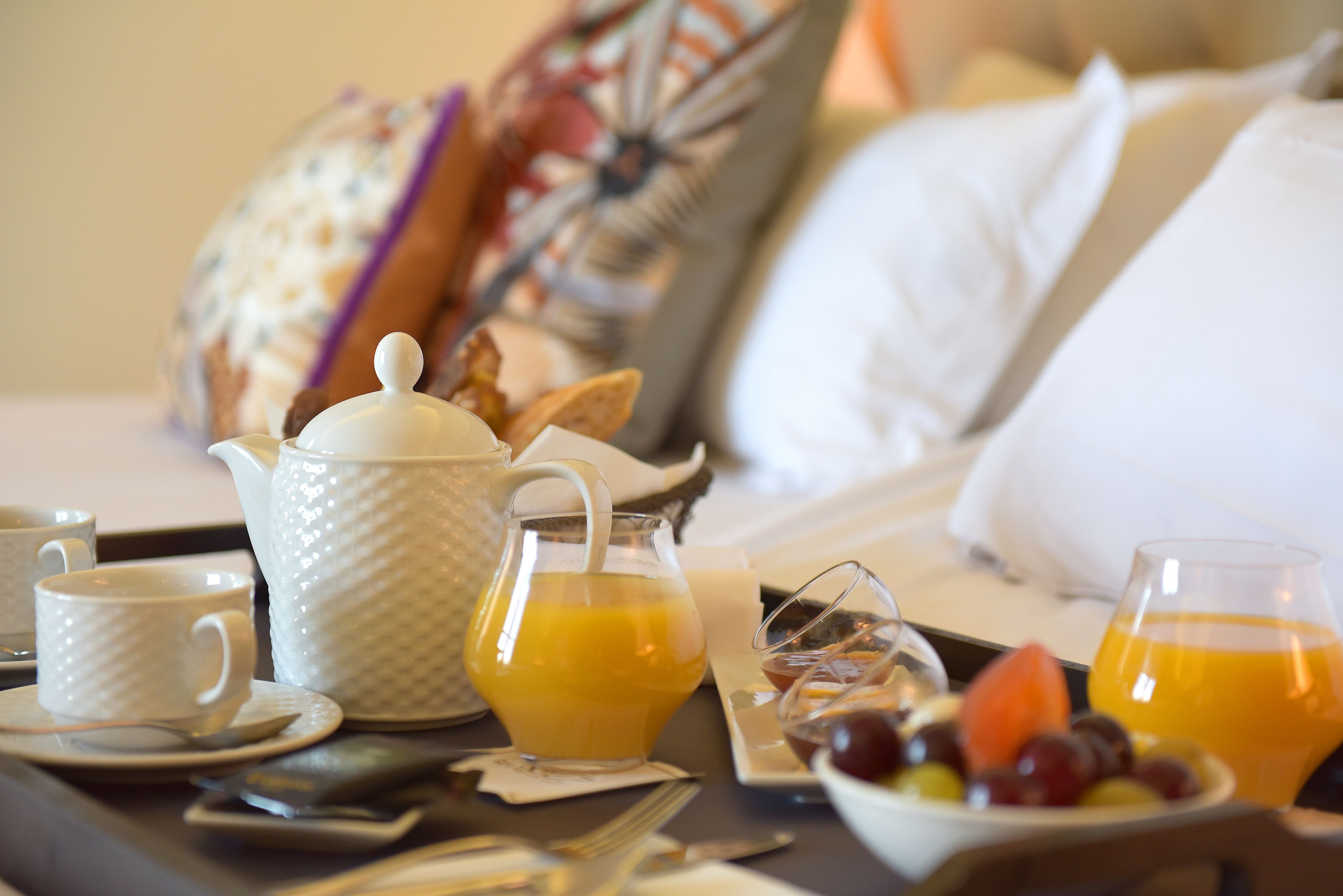 Un plateau de petit-déjeuner avec une théière, des tasses et un panier de fruits, posé sur un lit.
