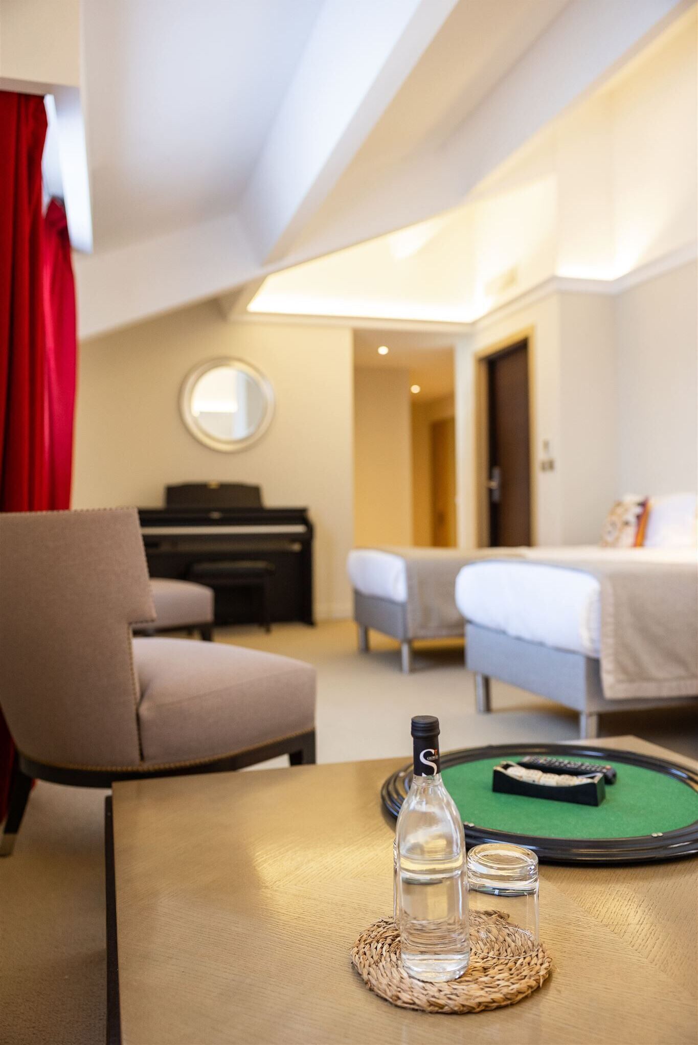 A hotel room with a piano, a bed, a table with a bottle and glass, and a green mat.