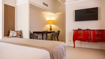 A hotel room with a bed, a desk with a lamp, a TV, and a red dresser.