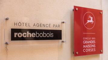 Deux panneaux sur un mur : l’un indique « Hôtel Agence Par rochebobois » et l’autre « Cercle des Grandes Maisons Corses ».