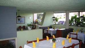 A restaurant with booths and tables, some with yellow napkins. There are plants and a window with a view of the outside. - Motel La Fortuna (Fresnillo)