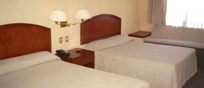 Ett hotellrum med två separata sängar, ett nattduksbord med en lampa, ett litet bord med en telefon och ett fönster med gardiner.