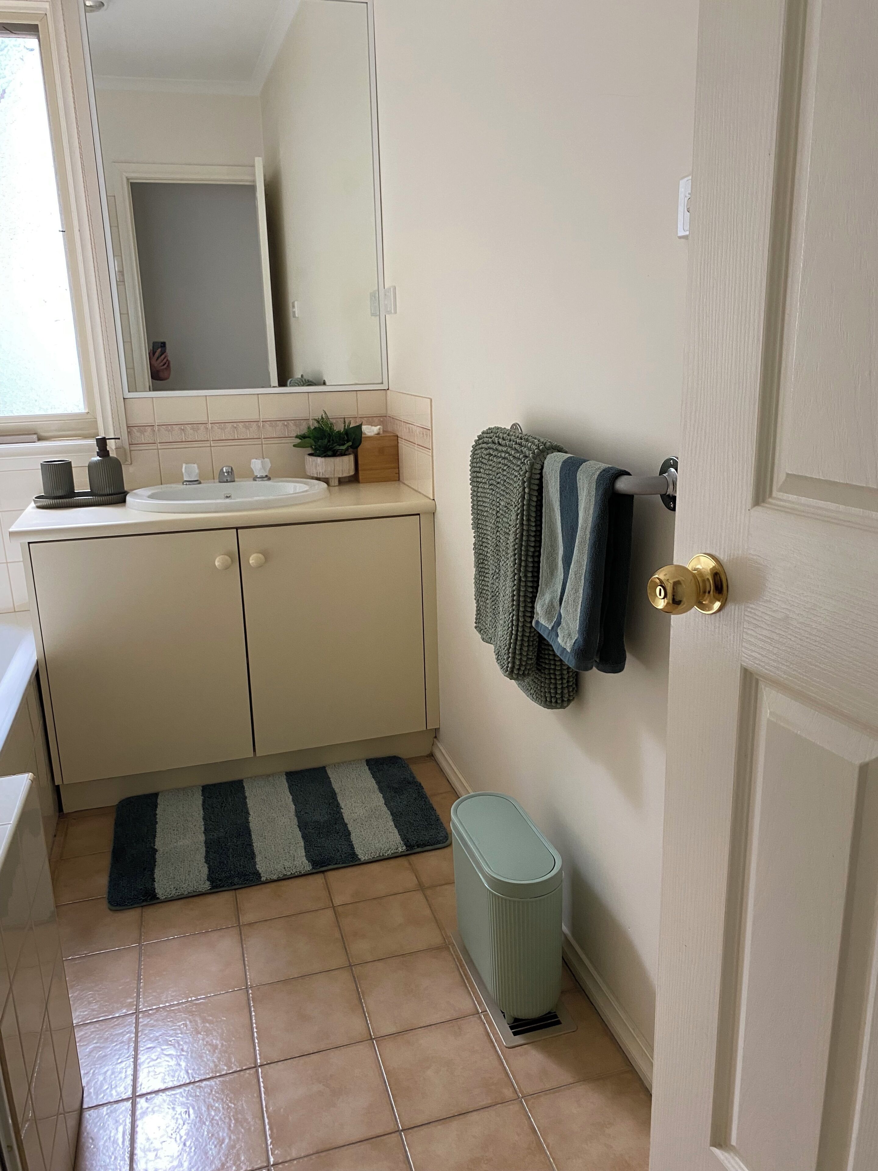 Un baño con lavamanos, espejo, toallero y cubo de basura.