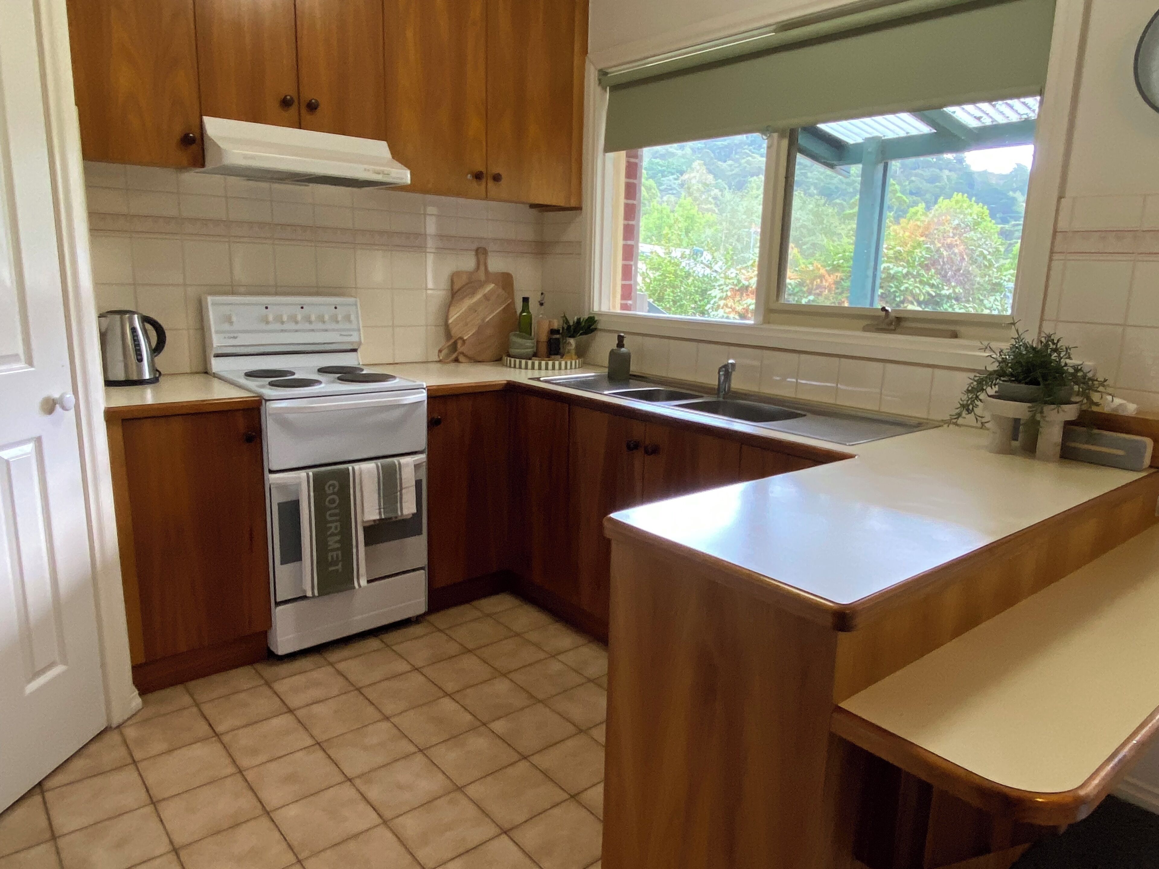 A kitchen with wooden cabinets, a white stove, a sink, and a window with a view of greenery.