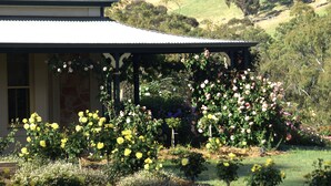 A house with a covered porch, surrounded by a garden with various flowering plants. - Battunga Cottages (Watervale)
