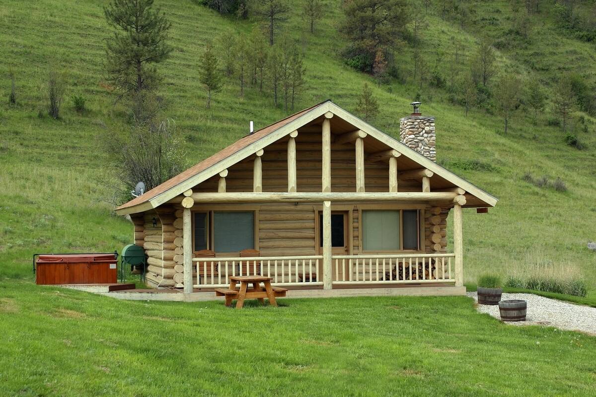 A log cabin with a porch, a hot tub, and a picnic table.