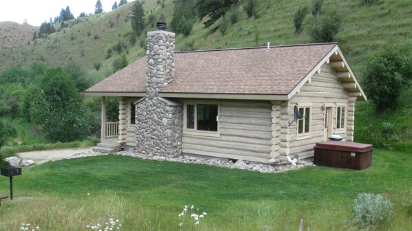 A log cabin with a stone chimney, a porch, and a small deck.