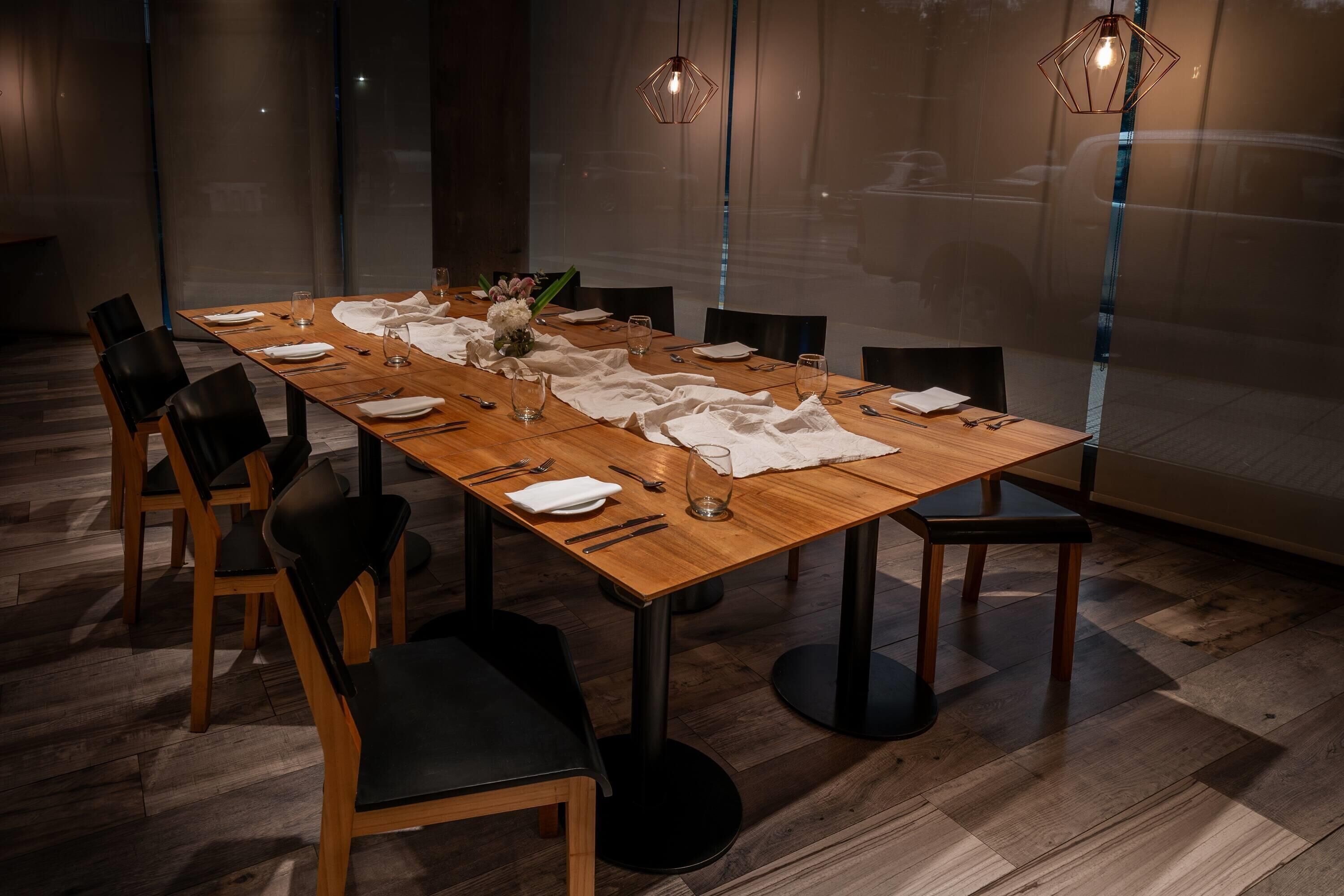 A dining room with a long wooden table set for six, surrounded by black chairs.