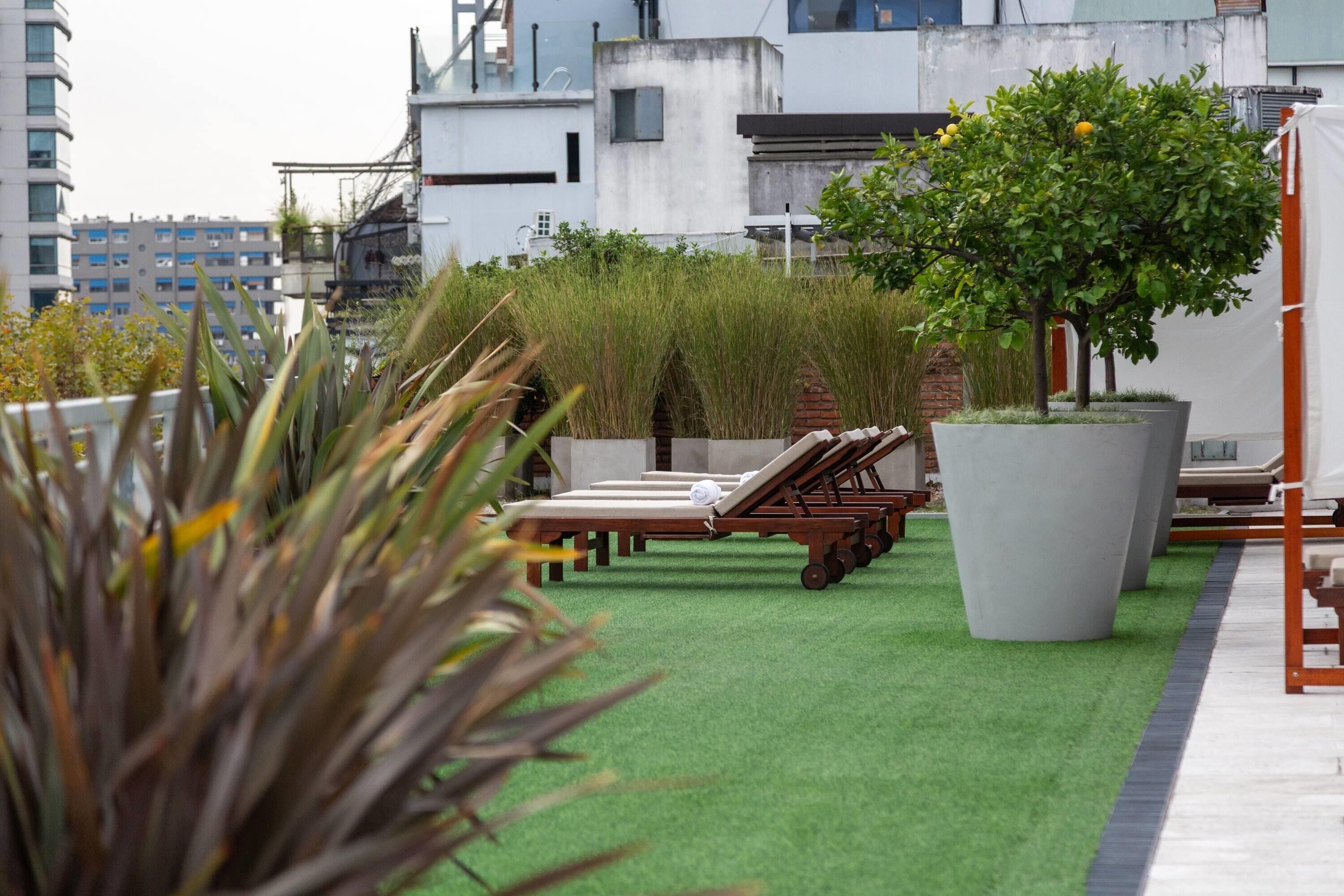 A rooftop terrace with artificial grass, lounge chairs, and a large planter with a tree.