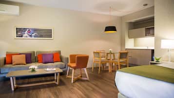 A modern living room with a sofa, coffee table, and chairs. There is a dining table with chairs, a bed, and a kitchen area with a sink and cabinets.