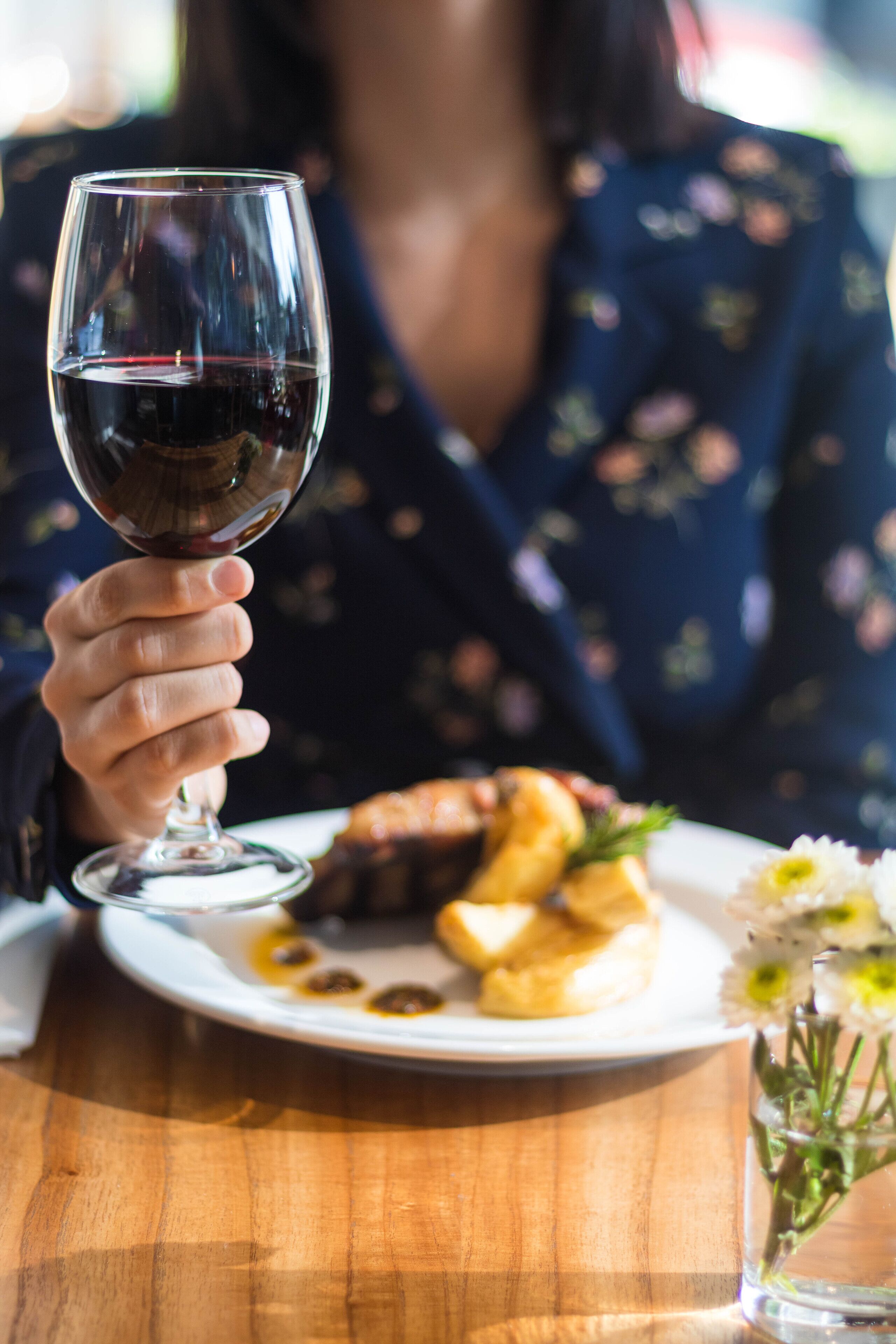 A person holding a wine glass with a plate of food in front.