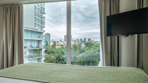 Ein Hotelzimmer mit großem Fenster, einem Bett mit grüner Bettdecke und einem an der Wand befestigten Flachbildfernseher.