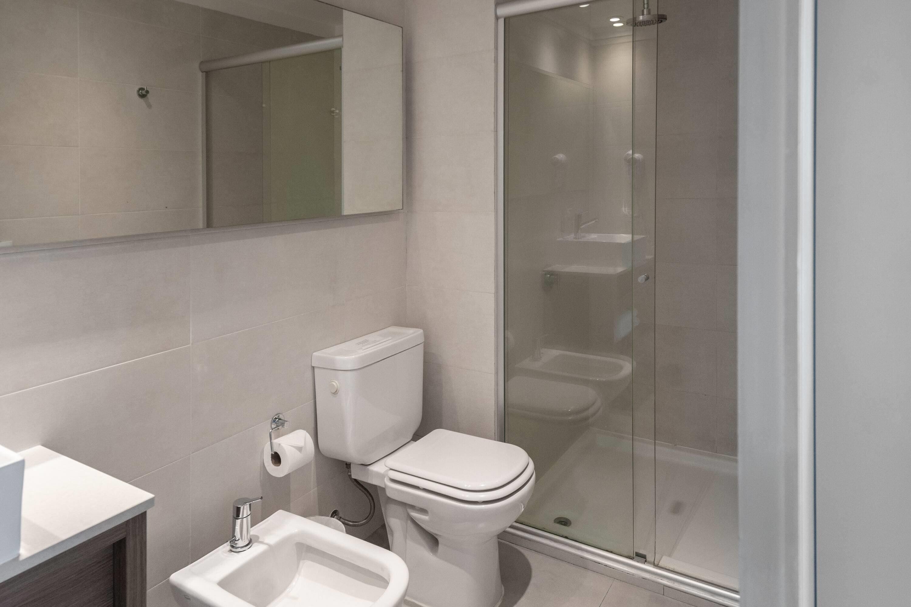 A modern bathroom with a toilet, bidet, and glass-enclosed shower.