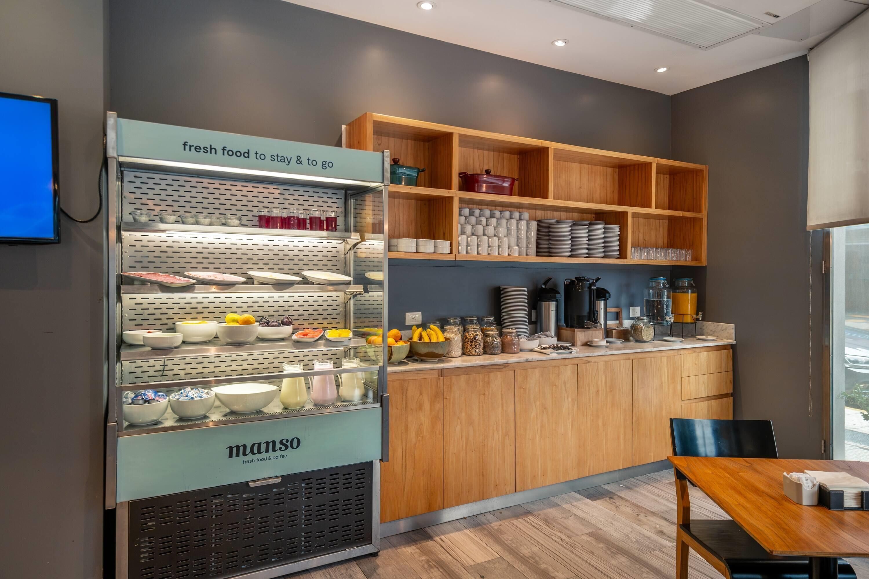 A modern kitchen area with a food display case, wooden shelves, and a dining table.